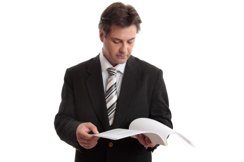 An individual in a suit and tie looks through a paper report.