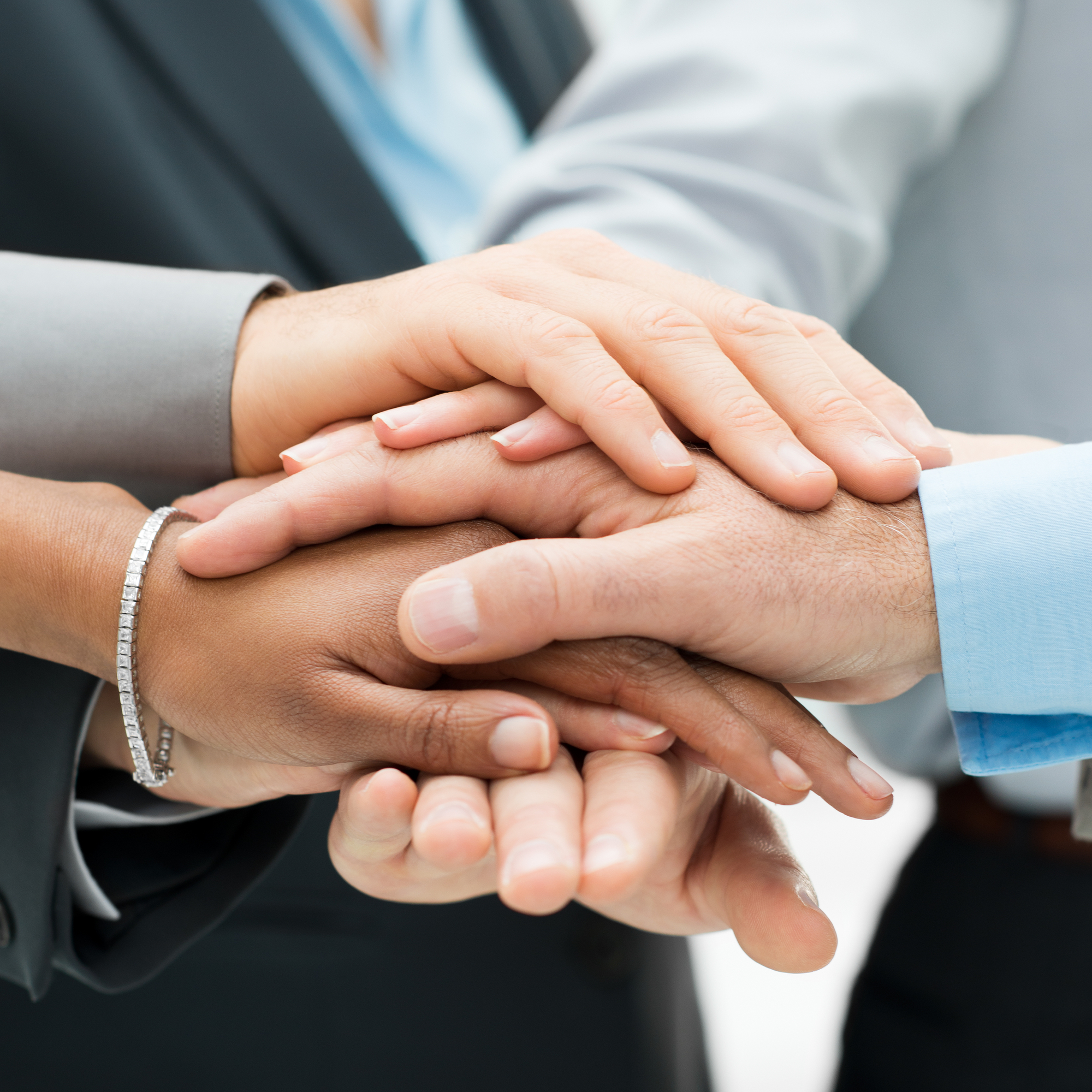 Close-up of a diverse group of workers’ hands resting on top of one another in a gesture of support.